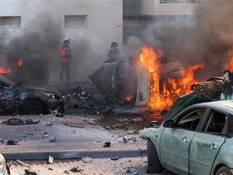 Las personas apagan incendios en coches tras un ataque con cohetes desde la Franja de Gaza en Ashkelon (Israel), el 7 de octubre de 2023. (Foto: AFP/VNA)