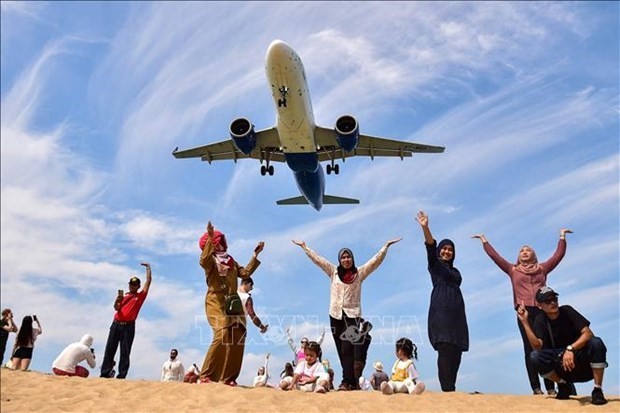 Turistas posan para una fotografía en la playa Mai Khao de Phuket mientras un avión aterriza en el aeropuerto internacional de Phuket (Foto: AFP/VNA)