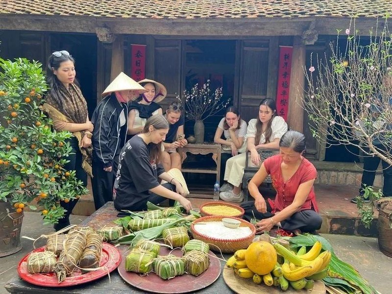 Los visitantes internacionales experimentan la envoltura de Banh Chung en la antigua aldea de Duong Lam. (Foto: VNA)