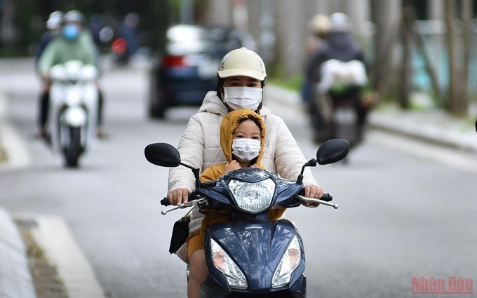 El enfriamiento del ambiente aconseja a los padres abrigar bien a sus hijos al desplazarse en la calle, pero también ponerles cascos para garantizar su seguridad. (Fotografía: Nhan Dan)